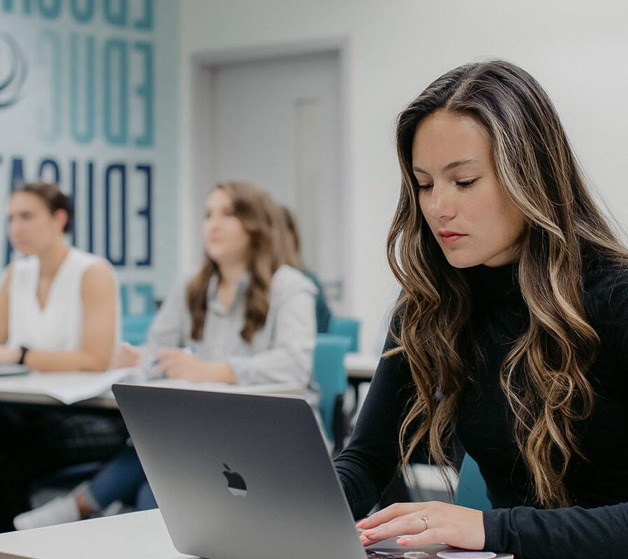 Students take notes on laptops during a lecture in a classroom.